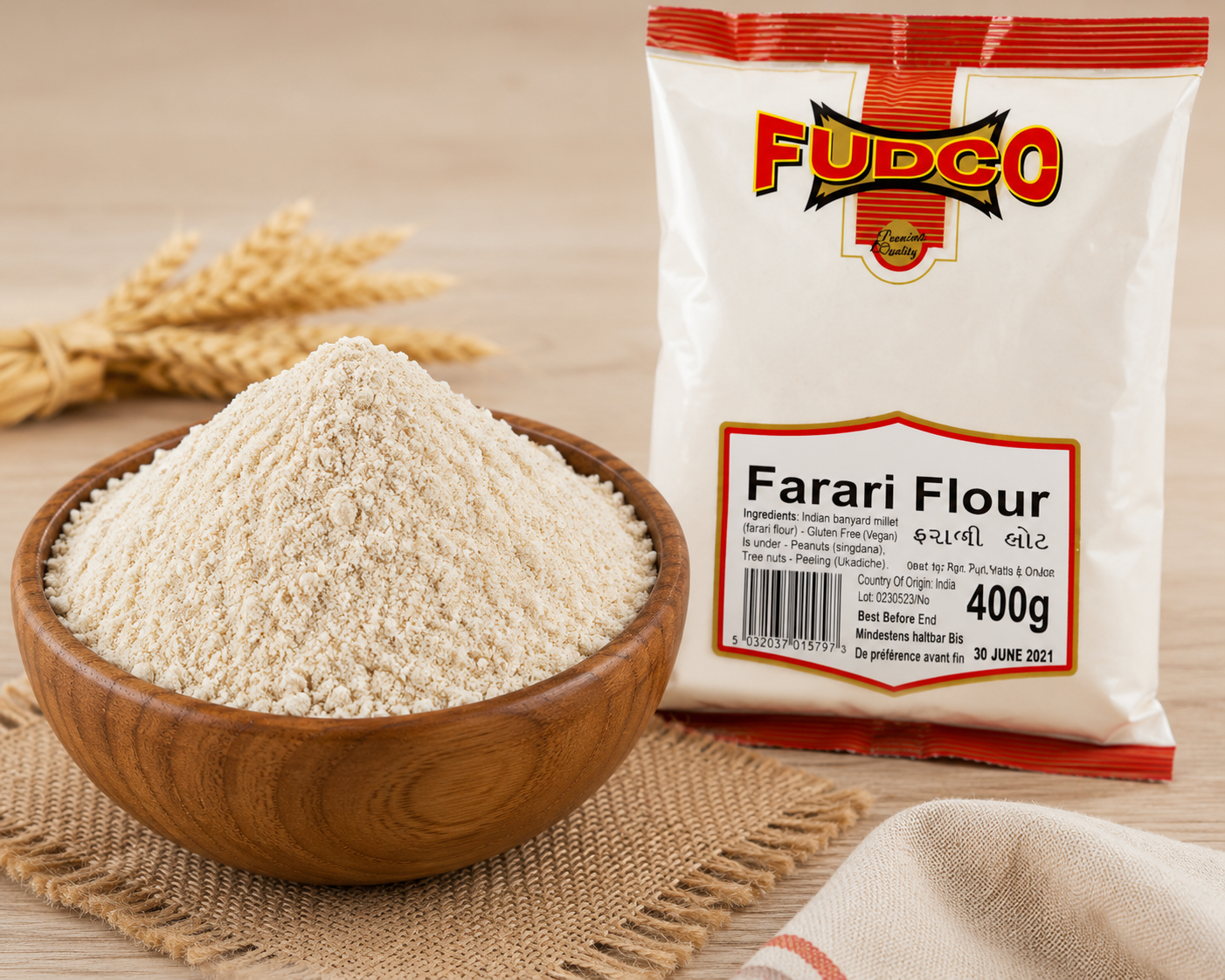 A 400g bag of Fudco Farari Flour next to a wooden bowl filled with the light beige flour, set on a burlap mat over a light wooden surface with wheat stalks in the background.