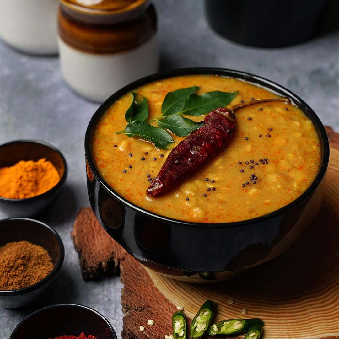 Bowl of yellow soup with spices and a red chili pepper on a gray surface