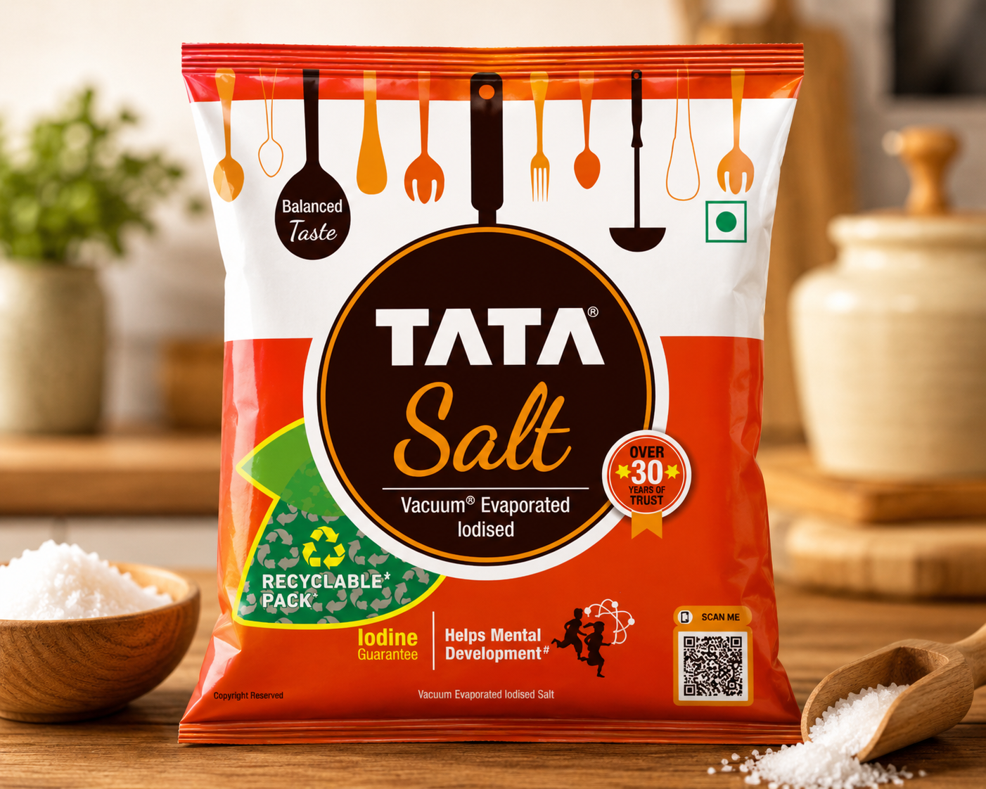 A bag of Tata Salt vacuum evaporated iodised salt stands on a wooden surface with bowls of salt and a spoon in the foreground, against a softly blurred kitchen background.