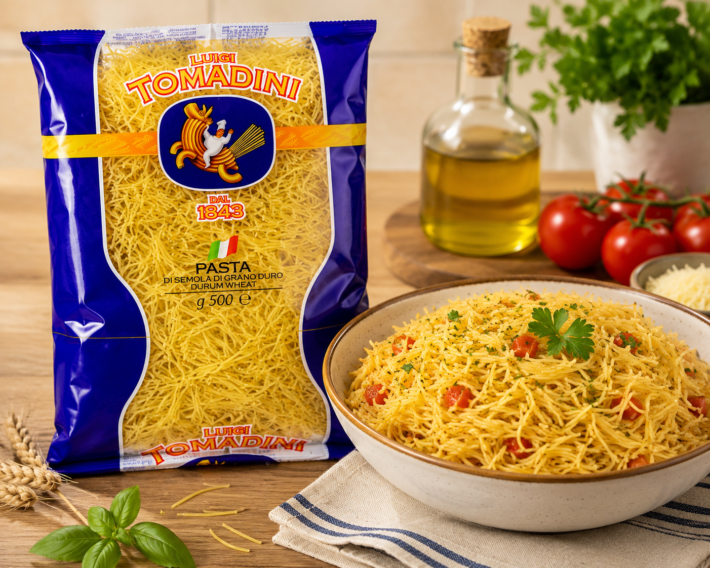 A bag of Il Maestro Tomadini spaghetti al taglio next to a bowl of prepared spaghetti with tomatoes and parsley, set on a wooden table with olive oil and fresh basil.