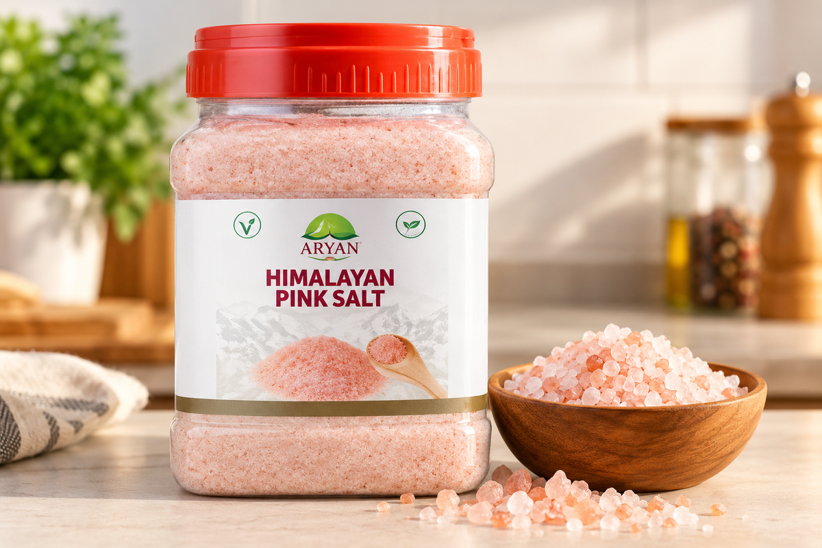 Aryan Himalayan Pink Salt 1kg jar displayed on a kitchen countertop beside a wooden bowl filled with coarse pink salt crystals, with scattered salt granules and a softly blurred kitchen background, ideal for showcasing pink salt for everyday cooking and seasoning.