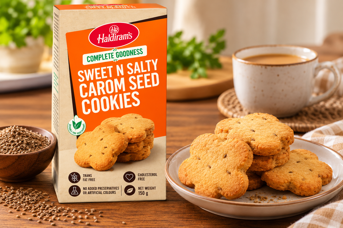 Haldiram’s Sweet N Salty Carom Seed Cookies 150g pack displayed with golden-brown cookies on a plate, carom seeds and a cup of tea on a wooden table.