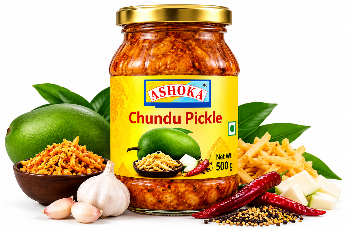 Ashoka Chundu Pickle 500g featuring a glass jar with a gold lid and yellow label, filled with traditional sweet and tangy shredded mango pickle, alongside fresh green mangoes, raw mango slices, leafy greens, red chillies, mustard seeds, and aromatic Indian spices.