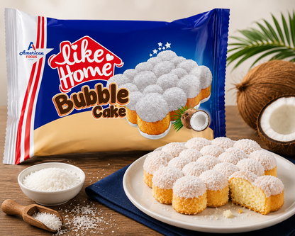 A package of Like Home Bubble Cake by American Foods is shown alongside several small golden sponge cakes dusted with white coconut powder on a white plate, with whole and halved coconuts, a bowl of coconut powder, and a wooden spoon on a wooden surface.