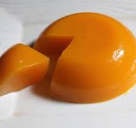 A close-up of a bright orange-yellow translucent gel or candy piece on a white surface, with a small separate piece in front.