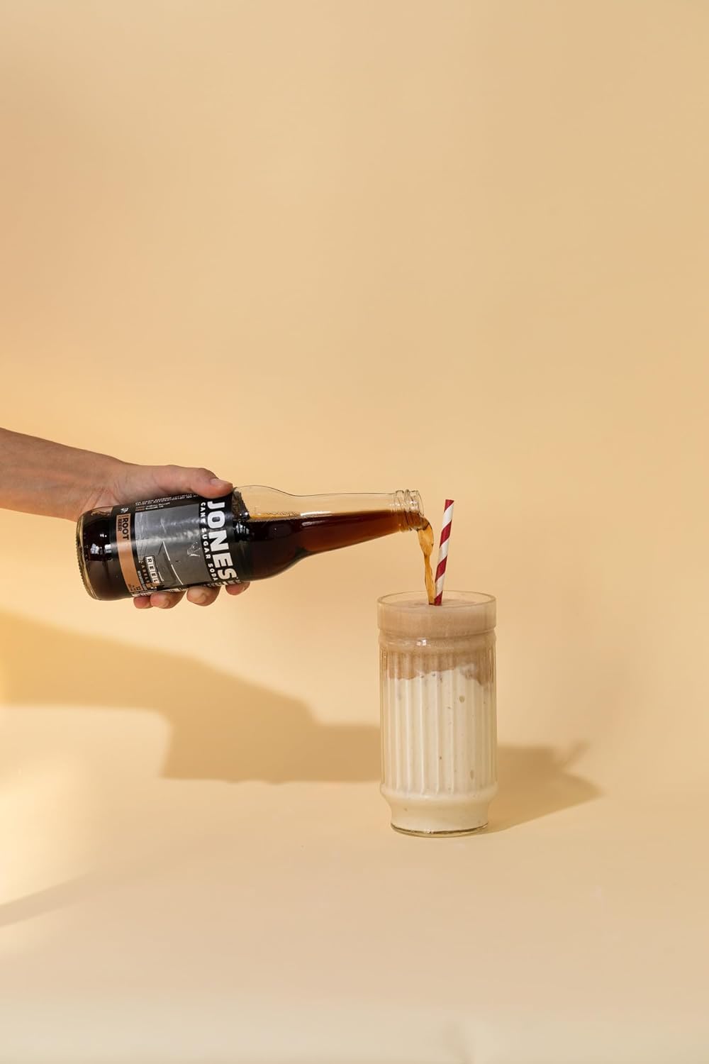 A 355ml glass bottle of Jones Soda Root Beer standing upright, filled with dark brown soda and sealed with a metal cap. The bottle features the bold Jones Soda logo and a rotating photo label that highlights the brand’s playful, craft-soda style.