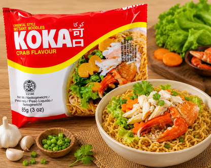 A package of KOKA Crab Flavour Instant Noodles shown next to a bowl of prepared noodles topped with crab meat, lettuce, and carrots on a wooden table with fresh ingredients around it.