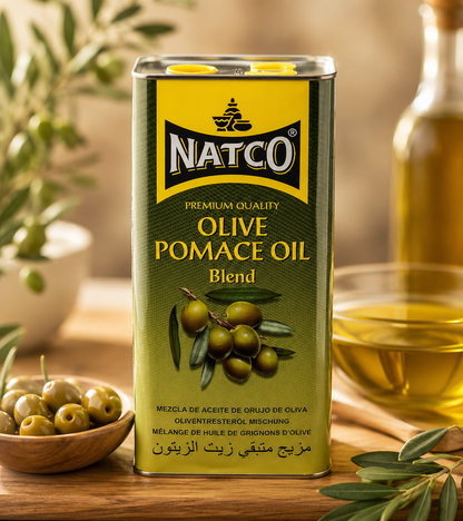 Natco Olive Pomace Oil Blend metal tin displayed on a wooden kitchen countertop with fresh green olives, olive branches, a bowl of olive oil, and a blurred warm kitchen background, showcasing premium cooking oil.
