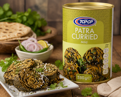 A can of Top of Patra Curried Mild (350g) standing next to a plate of prepared rolled curries garnished with parsley and cheese, set on a rustic wooden table with flatbread and onions in the background.