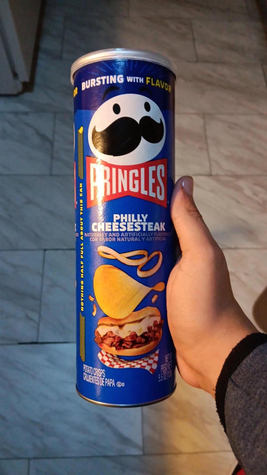 A canister of Pringles Philly Cheesesteak flavor, showcasing stackable, crispy chips with a savory, cheesy, and slightly peppery seasoning. The packaging features the iconic Pringles logo and highlights the Philly Cheesesteak flavor with vibrant graphic