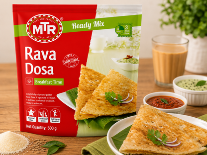 A 500g bag of MTR Ready Mix Rava Dosa (Breakfast Time) shown on a wooden table with prepared food props including a plate of dosas, a bowl of red chutney, and a glass of milk.