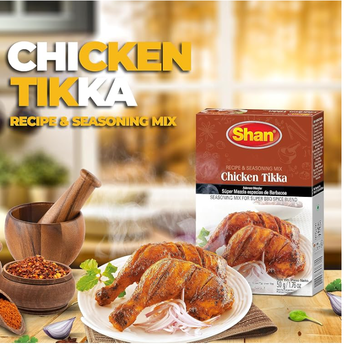 Shan Chicken Tikka Recipe & Seasoning Mix box shown beside cooked chicken pieces, onions, spices, and a mortar and pestle on a wooden surface, with large text reading 'CHICKEN TIKKA' and 'Recipe & Seasoning Mix'.