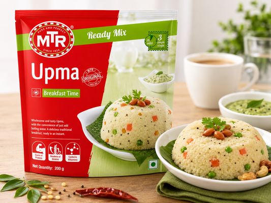 A package of Mirzade's Upma Ready Mix breakfast mix is shown on a wooden table next to a bowl of prepared upma with peanuts and coriander, with a cup of tea and a bowl of chutney in the background.