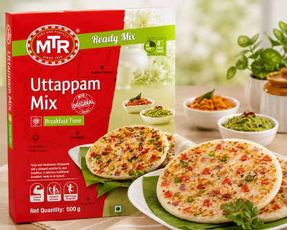 MTR Uttappam Mix ready mix food packaging box shown next to prepared Uttappam discs on plates with garnish and small bowls of chutney in a bright kitchen setting.