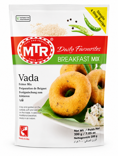 A 200g bag of MTR Daily Favourites Breakfast Mix (Vada) on a clean white background. The packaging features a white base with a prominent red and green logo band, accompanied by illustrations of raw ingredients (rice, peas) and a photo of golden-brown prepared vadas on a plate.