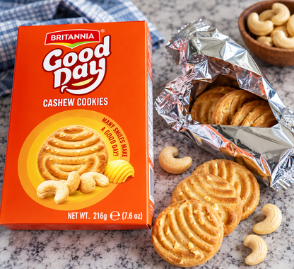 Britannia Good Day Cashew Cookies 216g box beside an opened silver foil packet with golden cookies and cashew nuts on a countertop.