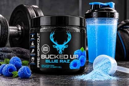 Bucked Up Blue Raz Pre-Workout Powder 290g displayed in a gym setting with blue shaker bottle, dumbbells, blue raspberries and pre-workout powder scoop.