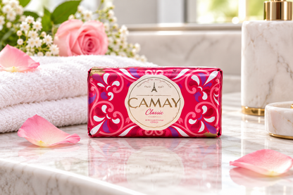 Camay Classic Soap in pink and red floral packaging displayed on a marble bathroom counter with pink rose petals, fresh roses and a soft white towel in a bright, elegant setting.