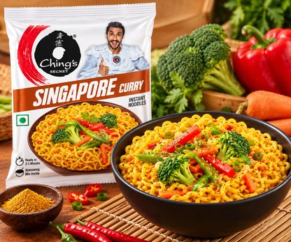 Ching’s Secret Singapore Curry Instant Noodles 60g packet displayed beside a black bowl of freshly prepared golden curry noodles with broccoli florets, red and green bell peppers, carrots, and fresh herbs. The white packet features the Ching’s Secret logo, Singapore Curry branding, a bowl-of-noodles illustration, and a smiling man giving a thumbs-up. Fresh vegetables, red chillies, curry seasoning, and wooden chopsticks arranged on a warm wooden surface create an inviting food photography scene.