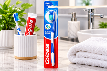 Colgate Extra Clean toothbrush displayed beside a white ceramic toothbrush holder, toothpaste and a folded white towel on a clean modern bathroom countertop.