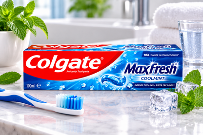 Colgate MaxFresh Coolmint Toothpaste 100ml displayed on a clean marble bathroom counter beside a blue and white toothbrush, fresh mint leaves, ice cubes and a glass of water.
