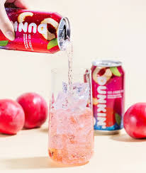 DUNKIN Zero Sparkling Plum can next to fresh plums, showcasing natural plum-inspired flavor in a sparkling soda.