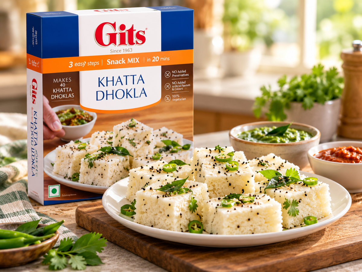 Gits Khatta Dhokla Mix 200g box displayed beside a plate of soft, steamed Gujarati dhokla garnished with mustard seeds, green chillies and coriander, served with green and red chutneys on a warm kitchen counter.