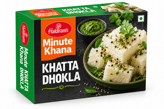 Haldiram’s Minute Khana Khatta Dhokla 283g box featuring green, orange and black packaging, soft white dhokla garnished with mustard seeds and fresh coriander, served with green chutney.