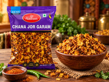 Haldiram’s Chana Jor Garam snack packet displayed beside a wooden bowl of crispy spiced chickpea flakes, with green chillies and Indian spices on a rustic wooden table.