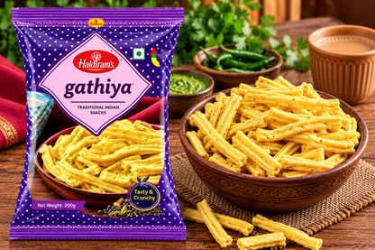 Haldiram’s Gathiya snack packet displayed beside a wooden bowl filled with golden, crispy gathiya sticks, with green chillies, chutney and a cup of tea on a rustic wooden table.