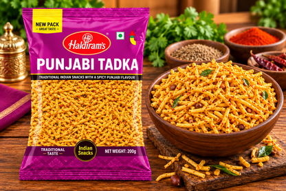 Haldiram’s Punjabi Tadka snack packet displayed beside a wooden bowl of golden spicy sev, with red chilli, whole spices and fresh herbs on a rustic wooden table.