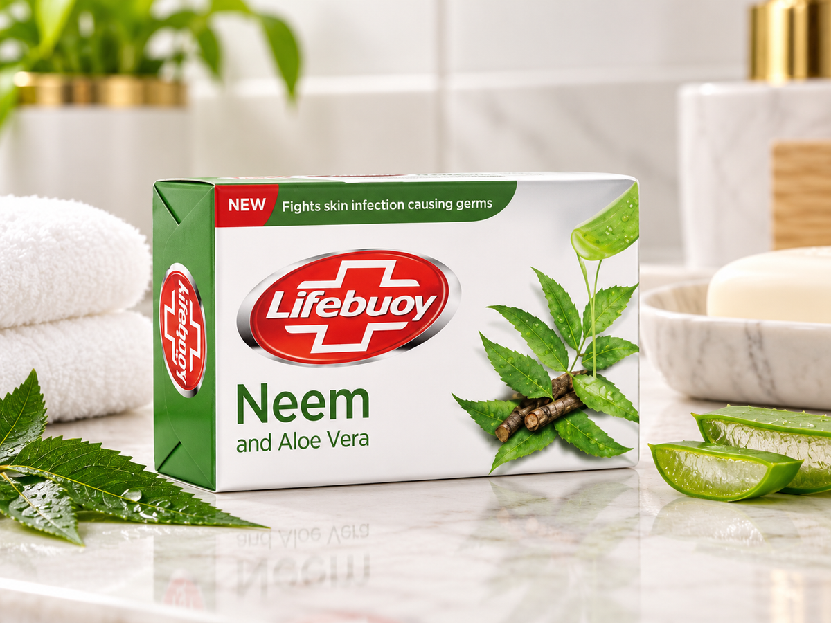 Lifebuoy Neem and Aloe Vera Soap 123g box displayed on a marble bathroom countertop beside fresh neem leaves, sliced aloe vera, a folded white towel, and a ceramic soap dish in a bright, natural bathroom setting.