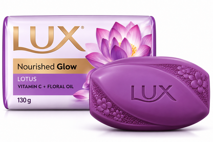 Lux Nourished Glow Lotus Soap 130g featuring a glossy purple oval soap bar embossed with the Lux logo, paired with elegant lavender and white packaging accented with gold lettering and beautiful pink and purple lotus flower illustrations. Displayed against a clean white background, showcasing the floral beauty soap enriched with vitamin C and floral oil for a nourishing bathing experience and soft, glowing-looking skin.