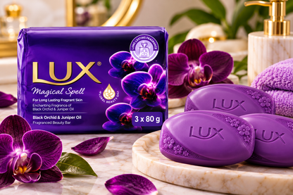Lux Purple Magical Spell Soap 3 Pack x 80g displayed alongside three glossy purple soap bars embossed with the Lux logo on a marble bathroom surface. The deep violet packaging features gold branding, purple orchid illustrations, and Black Orchid and Juniper Oil fragrance details, complemented by fresh purple orchids, scattered petals, a soft lavender towel, and elegant bathroom accessories in a luxurious spa-inspired setting.