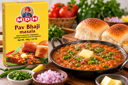 MDH Pav Bhaji Masala 100g packet displayed beside a hot pan of homemade pav bhaji, served with soft toasted bread rolls, butter, fresh coriander, chopped onions, green chilies, and lemon, showcasing the spice blend for preparing flavorful Indian vegetable curry.