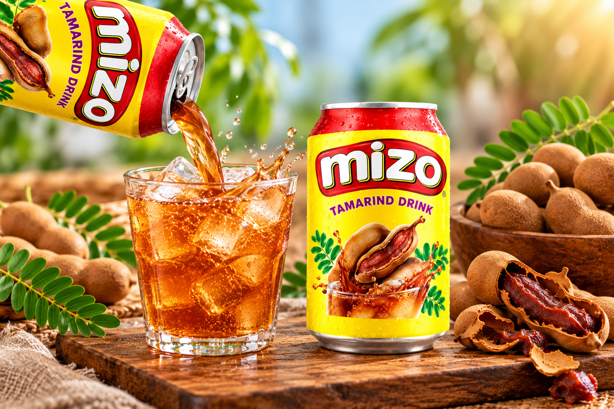 Mizo Tamarind Drink can pouring amber beverage into an ice-filled glass, with whole and split tamarind pods and green leaves.