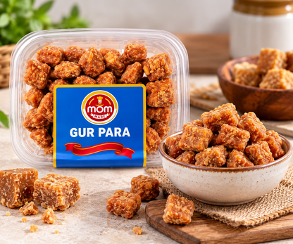 Mom Made Gur Para 300g container displayed beside a bowl of crunchy golden-brown gur para pieces on a rustic tabletop, with scattered jaggery snacks and natural kitchen décor.