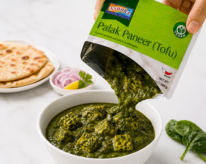 Ashoka Palak Paneer Tofu being poured into a white bowl, served with fresh chapati and spinach on a clean white background.