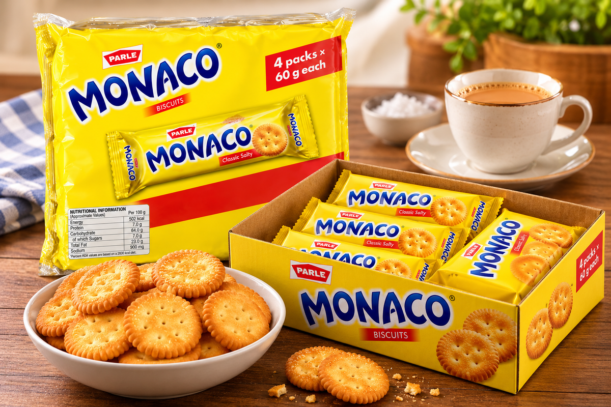 Parle Monaco Salted Biscuits multipack displayed with an open box of individual packets, a bowl of golden salted crackers and a cup of tea on a wooden table.