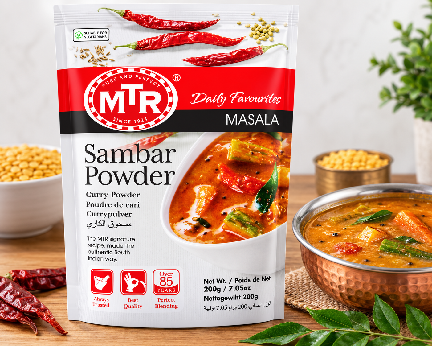 A package of MTR Masala Curry Powder prominently displayed on a wooden surface, surrounded by culinary props including a bowl of prepared curry, red chilies, chickpeas, and green leaves. The packaging features a red and white design with a photo of a spicy curry on the front.