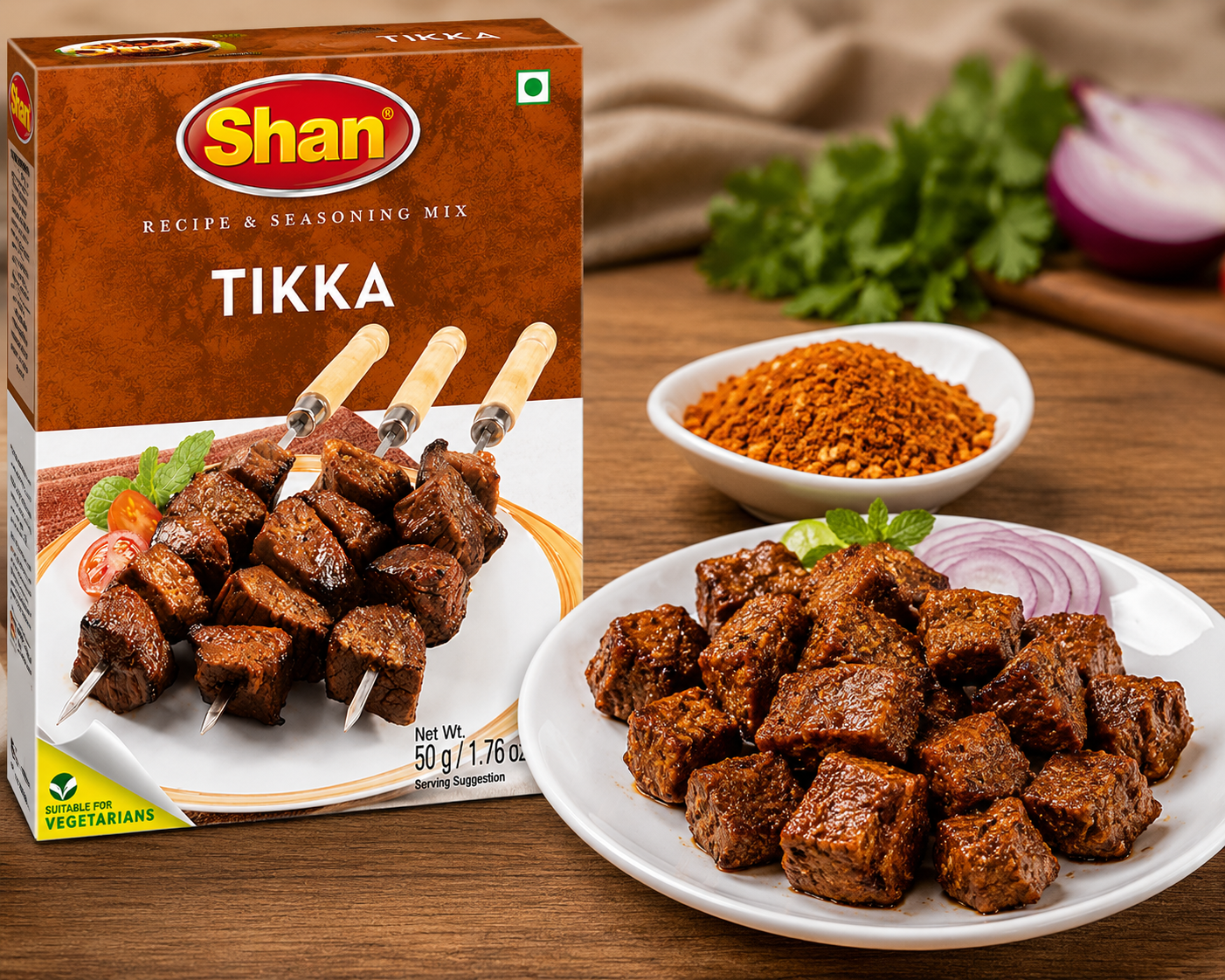 Shan Tikka Recipe & Seasoning Mix box shown beside plated cooked tikka pieces, a small bowl of reddish spice powder, and fresh herbs on a wooden surface.