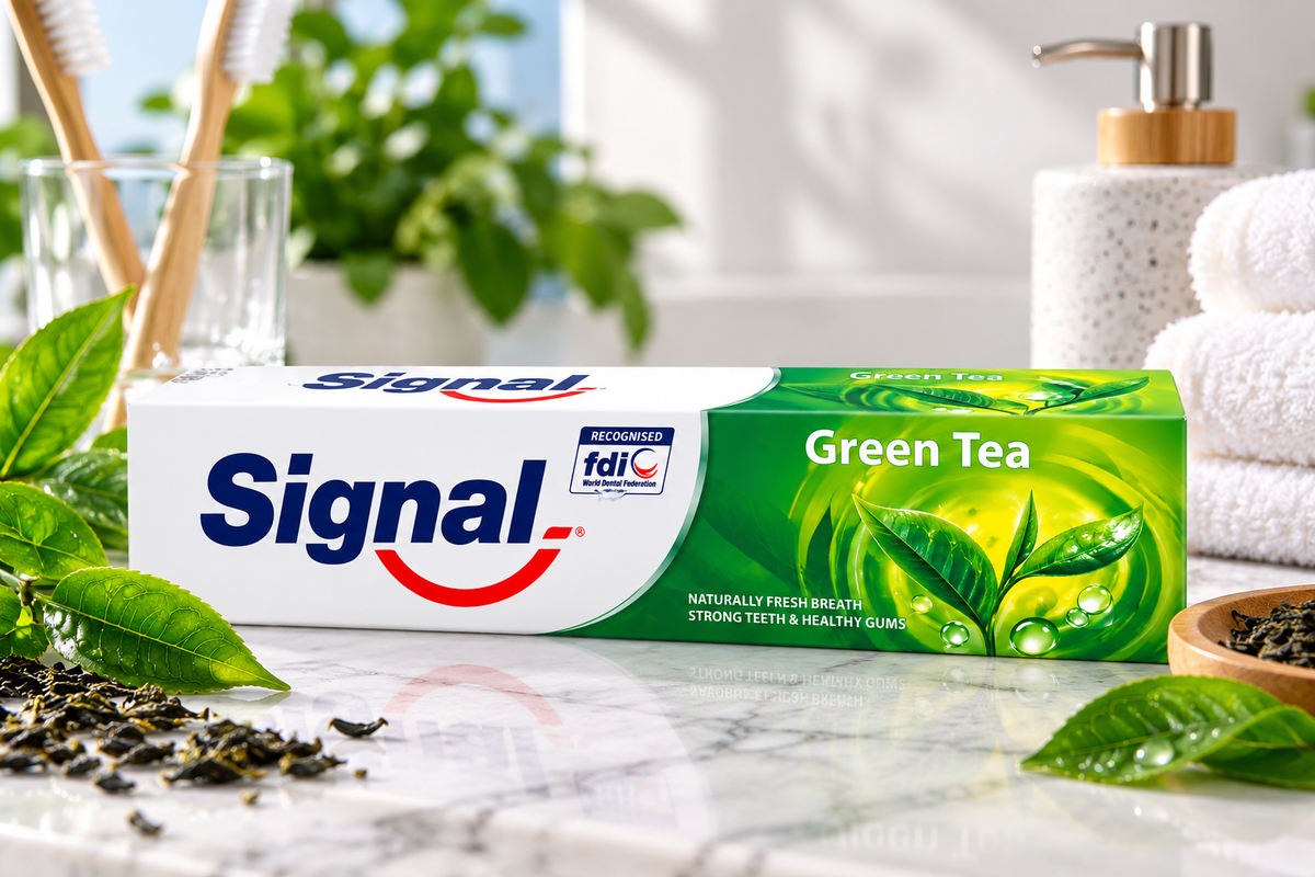 Signal Green Tea Herbal Toothpaste 100g displayed on a marble bathroom countertop with fresh green tea leaves, bamboo toothbrushes, a white towel, and a soap dispenser in a bright, natural bathroom setting.