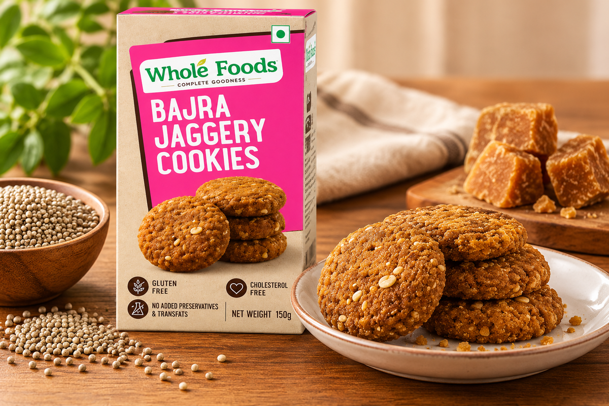 Whole Foods Bajra Jaggery Cookies 150g pack displayed with golden-brown cookies, bajra grains and jaggery pieces on a wooden table.